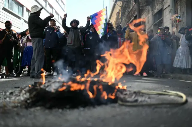 Un fuego pequeño en la calle y detrás hay varias personas paradas manifestando