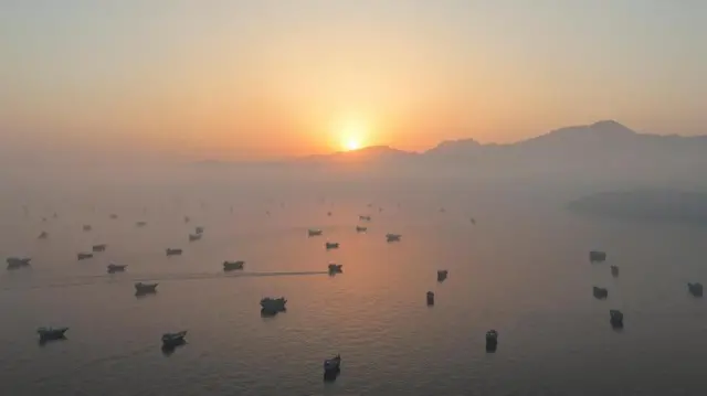 Muchas embarcaciones están fondeadas mientras sale el sol en el golfo de Omán.