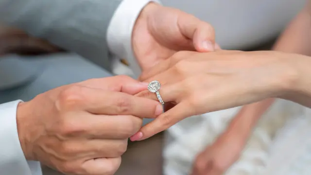 Un hombre coloca un anillo de compromiso con un diamante sintético en la mano de su pareja.