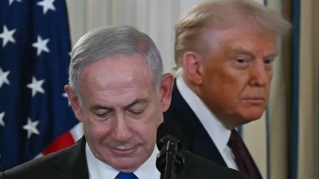 Donald Trump aparece detrás de Benjamin Netanyahu, que mira hacia abajo, durante una rueda de prensa en la Casa Blanca en 2025.