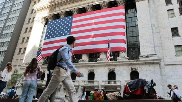 The New York Stock Exchange is seen during morning trading on May 26, 2026. A large American flag hangs from the front of the building and people walk in the street in front of it