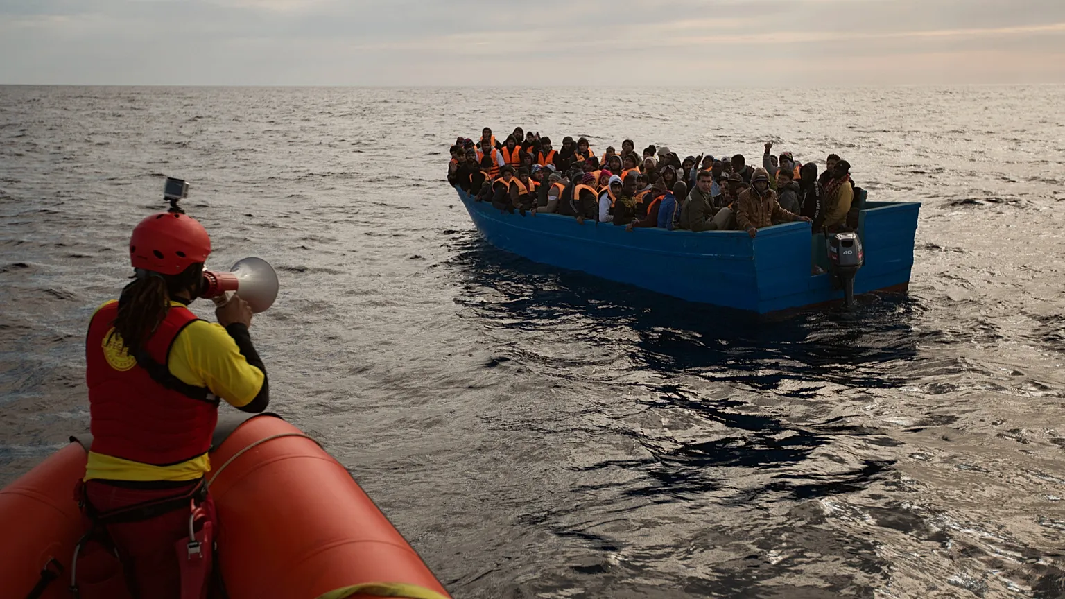 Migrants and refugees are assisted by members of the Spanish NGO Proactiva Open Arms, as they crowd aboard a boat sailing out of control in the Mediterranean Sea about 21 mile