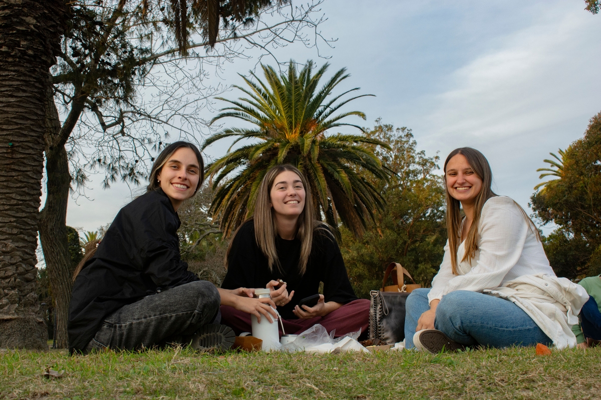 Tres jóvenes adultas disfrutan de un picnic al aire libre, creando un ambiente alegre y relajado (Pexels)