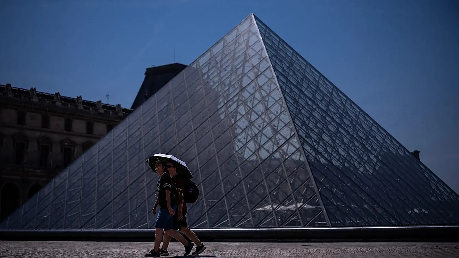 Tourists with an umbrella walk near the Louvre museum during a heat wave in Paris, Saturday, June 27, 2026.