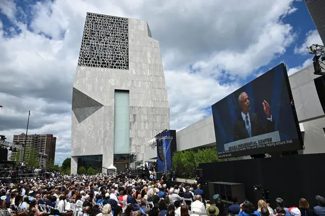 Obama dando su discurso frente a la torre del Centro. Hay una multitud escuchándolo y se ve al expresidente en una gran pantalla.