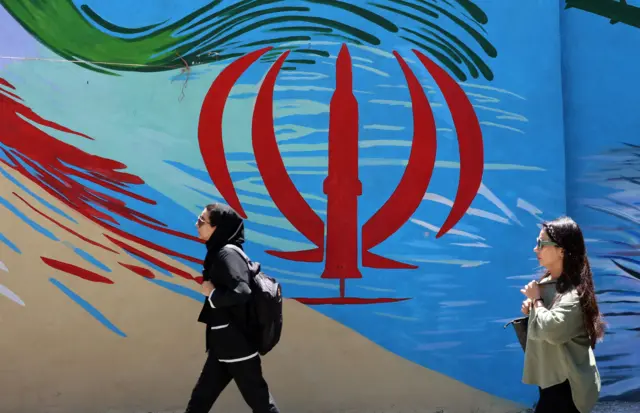 Dos mujeres iraníes pasan junto a una pintura mural con la bandera nacional de Irán en una calle de Teherán.