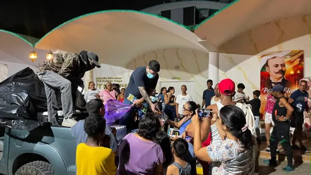 Víctor y su equipo entregando comida en La Guaira. Están montados en una camioneta rodeados de gente tomando fotos y recibiendo comidas.