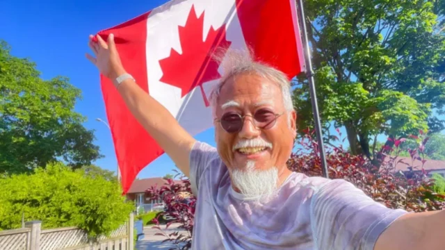 Dong Guangping posa frente a un departamento canadiense, con la bandera en la mano derecha.