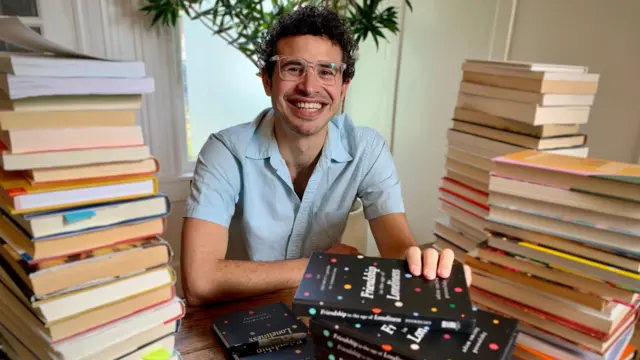 Adam Smiley Poswolsky sentado delante de una pila de libros.