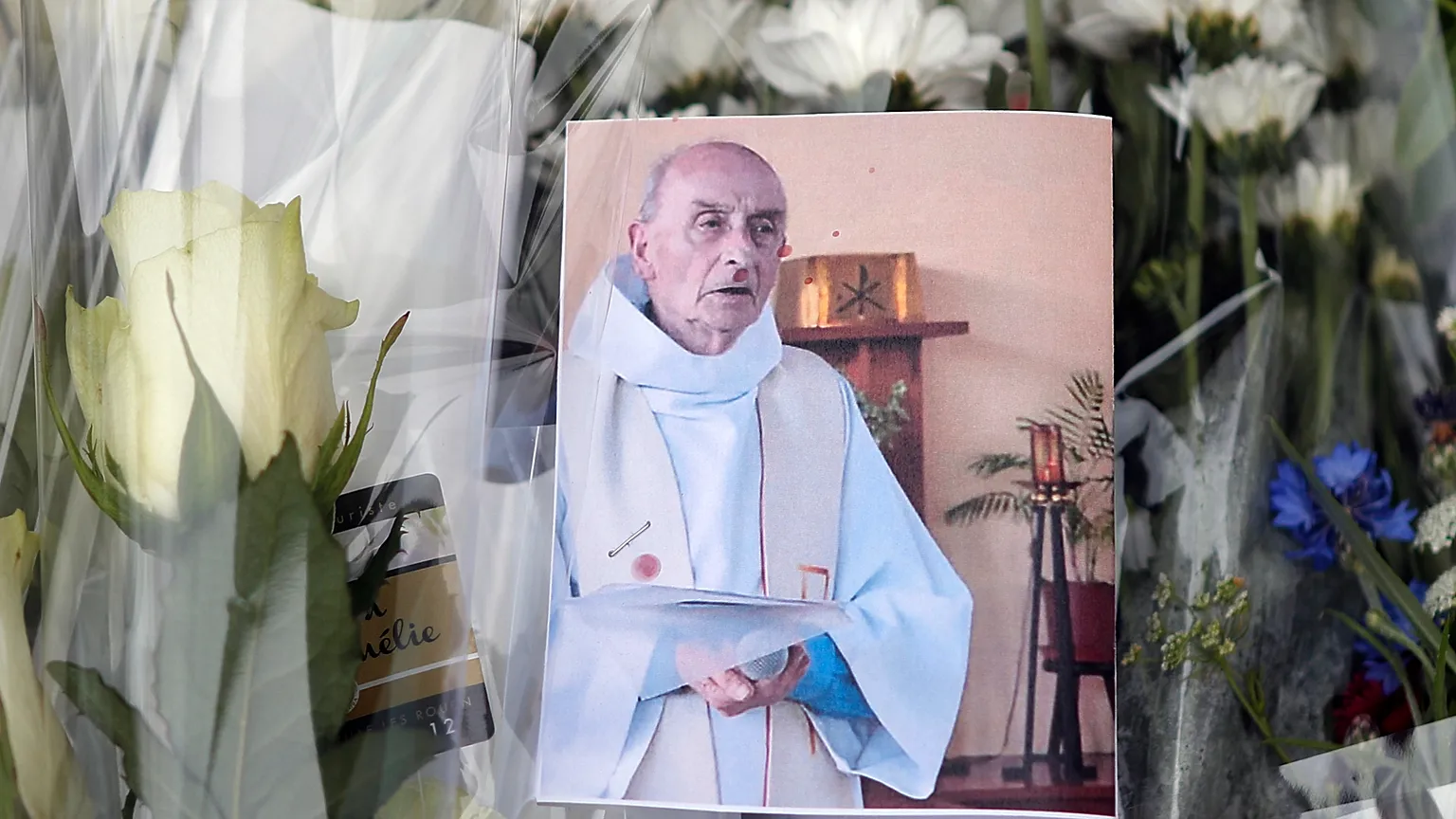 A photograph of Father Jacques Hamel is placed on flowers in front of the makeshift memorial, Saint-Étienne-du-Rouvray, 27 July 2016.