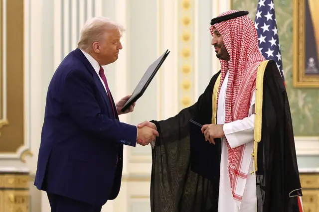 El príncipe Mohammed bin Salman saluda a Donald Trump, que sostiene una carpeta en su otra mano
