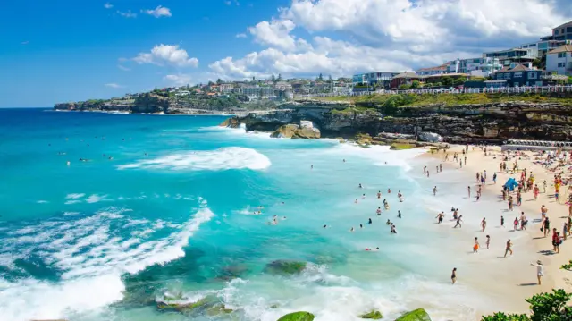 Playa de Sídney con aguas azules y cristalinas, la gente disfrura adentro y fuera del mar.
