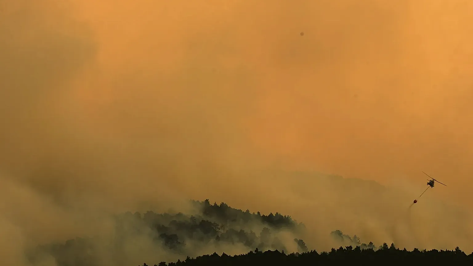 A firefighting helicopter drops water on the flames as a wildfire advances near Condemios de Arriba, Guadalajara province, Spain, Wednesday, July 22, 2026.