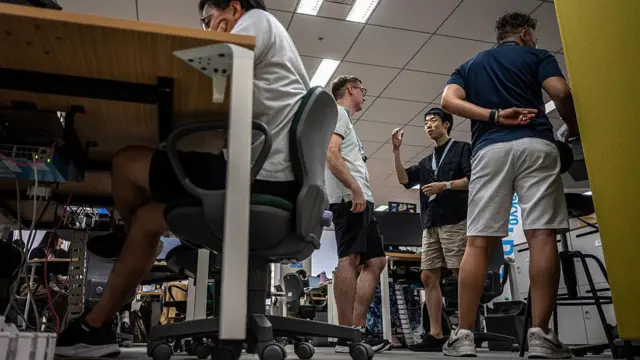 Cuatro hombres en pantalones cortos en una oficina en Tokio, Japón. Tres de ellos de pie, uno sentado con los codos apoyados en la mesa.