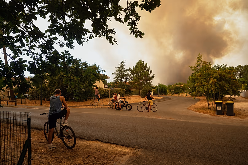 People watch massive plumes of smoke caused by wildfires in Le Porge, western France, Thursday, July 23, 2026.