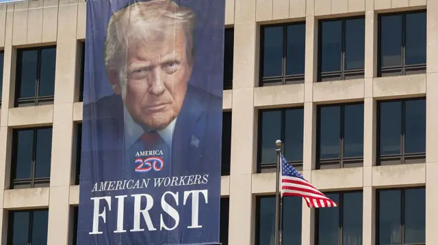 En el exterior del Edificio Frances Perkins del Departamento de Trabajo se lee en una pancarta con el retrato de Trump, "Trabajadores americanos primero".