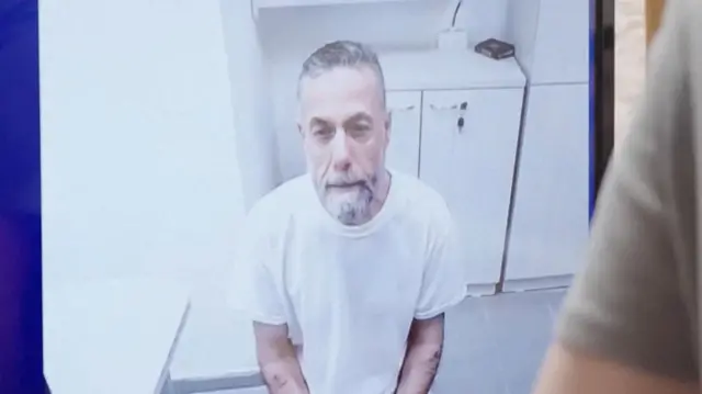 El médico palestino detenido, Hassam Abu Safiya, aparece en una pantalla vestido con una camisa blanca en prisión durante una audiencia ante la Corte Suprema israelí el 10 de junio de 2026.