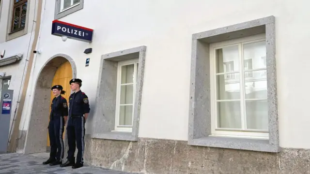Dos agentes de policía permanecen de pie frente a un edificio con un letrero de policía en alemán en la pared.