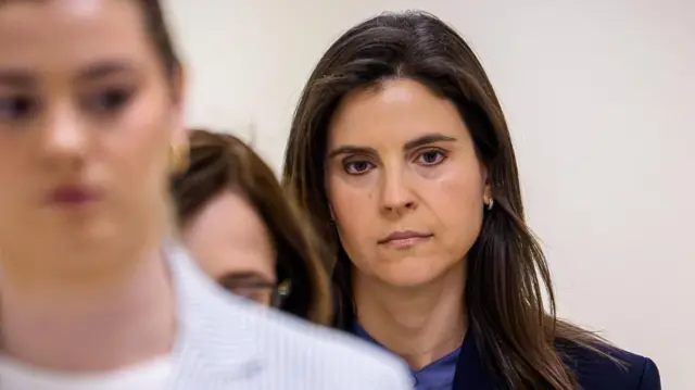 Sarah Kellen, una mujer de pelo largo castaño y vestida con un traje oscuro, mira fijamente al frente mientras camina con un grupo de otras mujeres por un pasillo anodino antes de prestar declaración ante el Congreso.