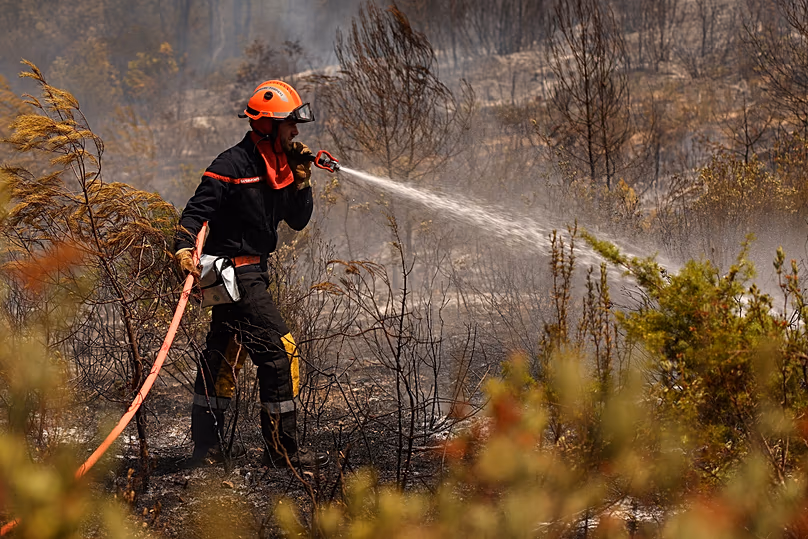 A firefighter sprays water on burnt vegetation and trees during clean up operations in an area affected by a wildfire in Cotignac, France, Wednesday July 22, 2026.