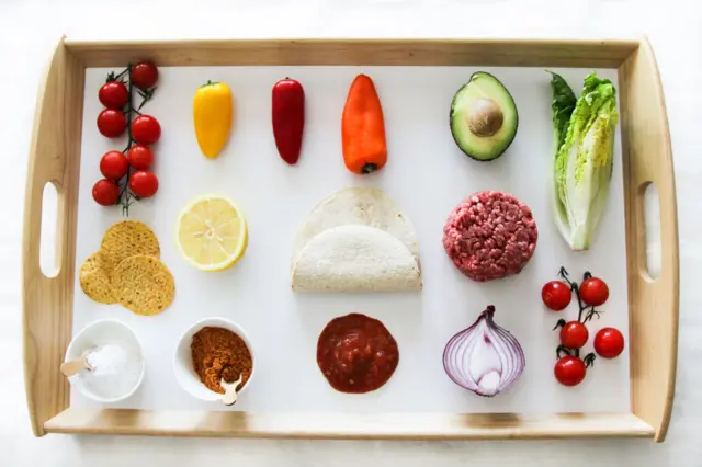 Una bandeja con los ingredientes basicos de unos tacos: tortillas, tomates, cebollas, carne molida, sal, lechuga.