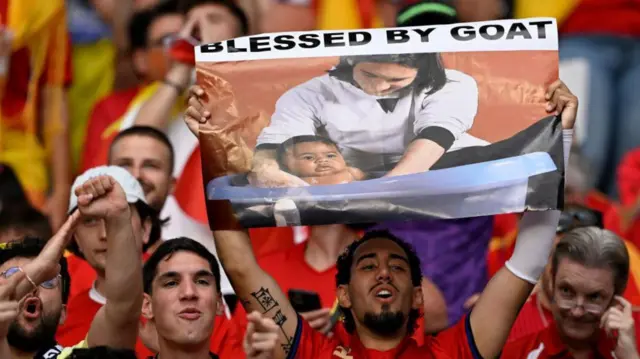 Fans de la selección española, uno de los cuales levanta un cartel con la foto de Messi y Lamine Yamal impresa.
