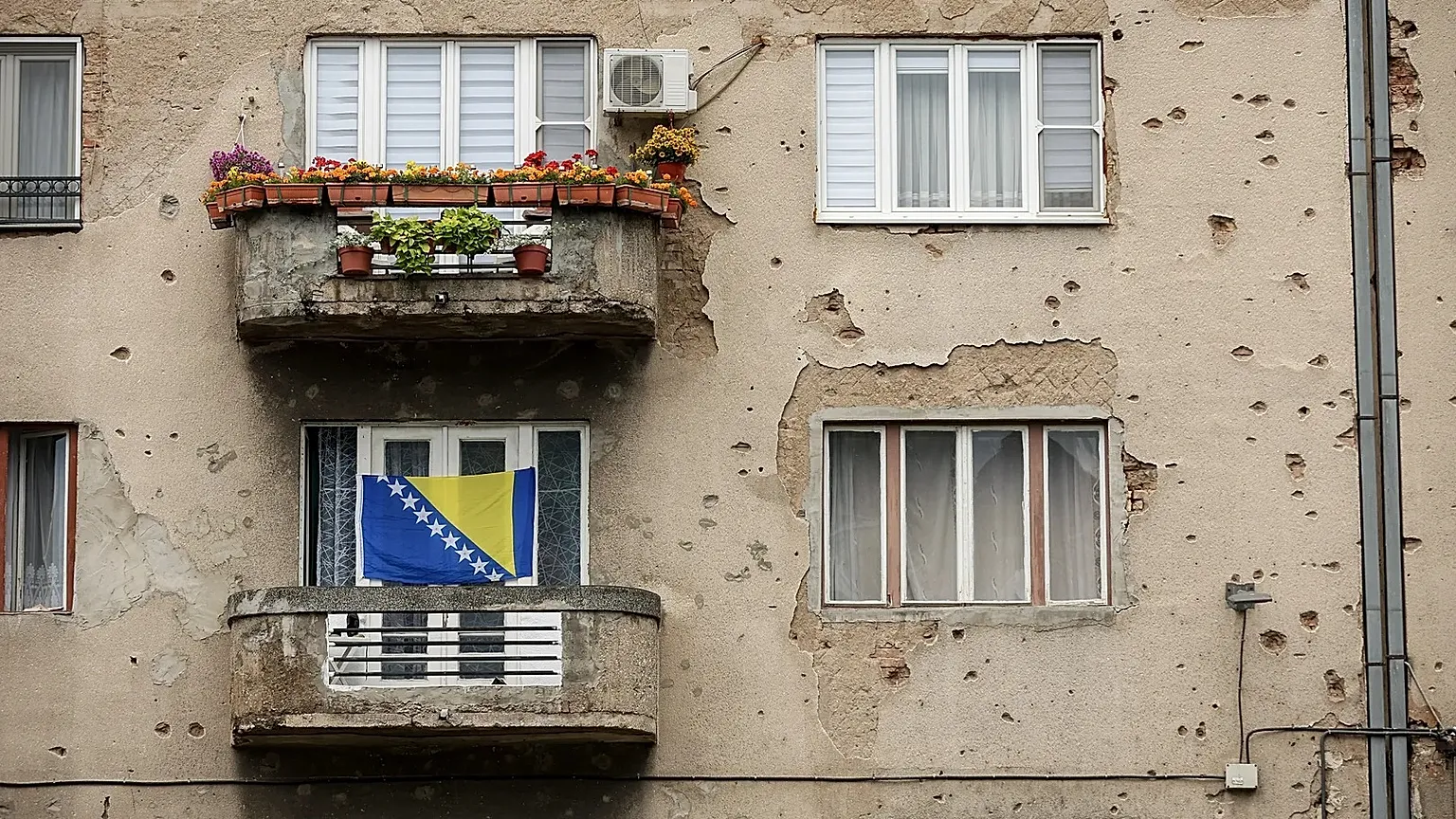 A Bosnian flag waves on a Sarajevo building scarred by bullet and shelling damage from the 1992-1995 war.