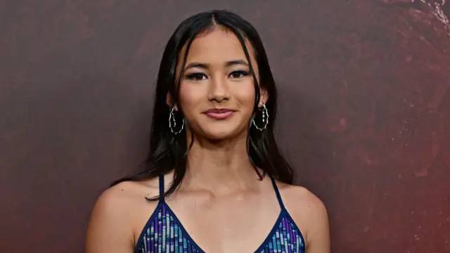Kaylee Hottle lleva un vestido brillante azul y morado y pendientes de aro plateados.