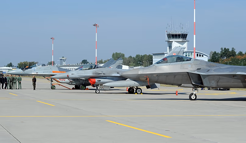 Officials walk past fighter jets parked on the apron, a Polish Air Force Mig-29, F-16, and F-22 Raptor at a military base in Lask, Poland, Aug. 31, 2015