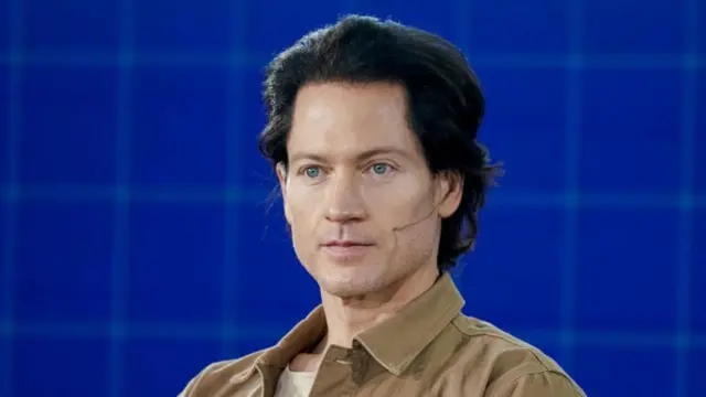 Bryan Johnson, fotografiado en 2021, luce el pelo oscuro peinado hacia atrás, ojos azules y lleva una chaqueta de color marrón claro.