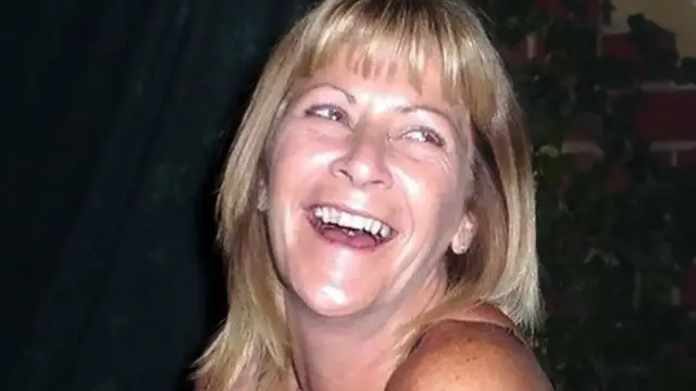Jean Hanlon mira ligeramente fuera de cámara. Tiene el cabello rubio hasta los hombros y se está riendo; se le ven los dientes superiores. Tiene los ojos claros. Solo se le ven los hombros, el cuello y la cabeza.