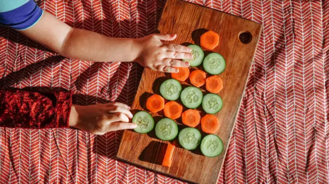 Trozos hexagonales de zanahoria y rodajas de pepino reposan sobre una tabla de cortar formando la forma de un pino.
