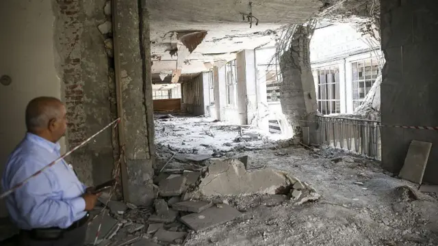 Un hombre observa los daños en el interior del Parlamento turco tras el ataque con helicópteros ocurrido el 15 de julio de 2016. Se aprecia un gran agujero en una pared, con ventanas destrozadas, cristales rotos y escombros esparcidos por todo el edificio.
