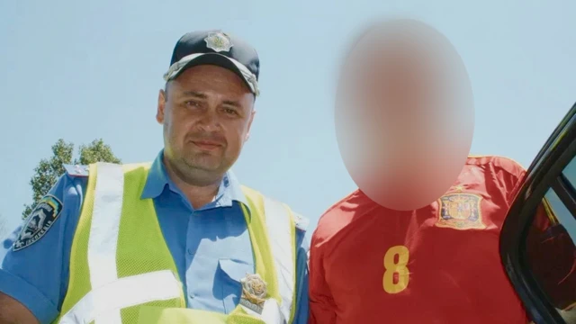 Temerbek aparece en la imagen con una gorra policial negra, una camisa de policía azul y un chaleco amarillo de alta visibilidad, mirando a la cámara con una leve sonrisa. A su lado se encuentra una persona con una camiseta de fútbol roja, cuyo rostro ha sido difuminado.