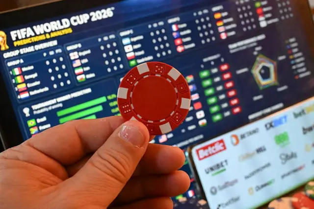 Ilustración de una ficha de casino sostenida frente a una pantalla que muestra datos de apuestas deportivas relacionados con la Copa Mundial de la FIFA 2026.