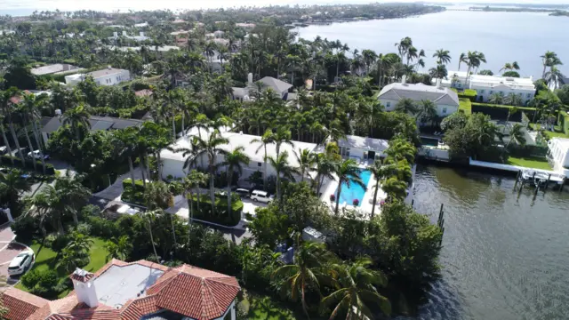 Vista aérea de la casa de Jeffrey Epstein en Palm Beach, que muestra una gran casa blanca en un barrio costero, con una piscina visible entre numerosas palmeras.
