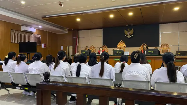 Dos filas de personas vestidas de blanco se sientan en bancos en una sala de audiencias, frente a un panel de jueces.